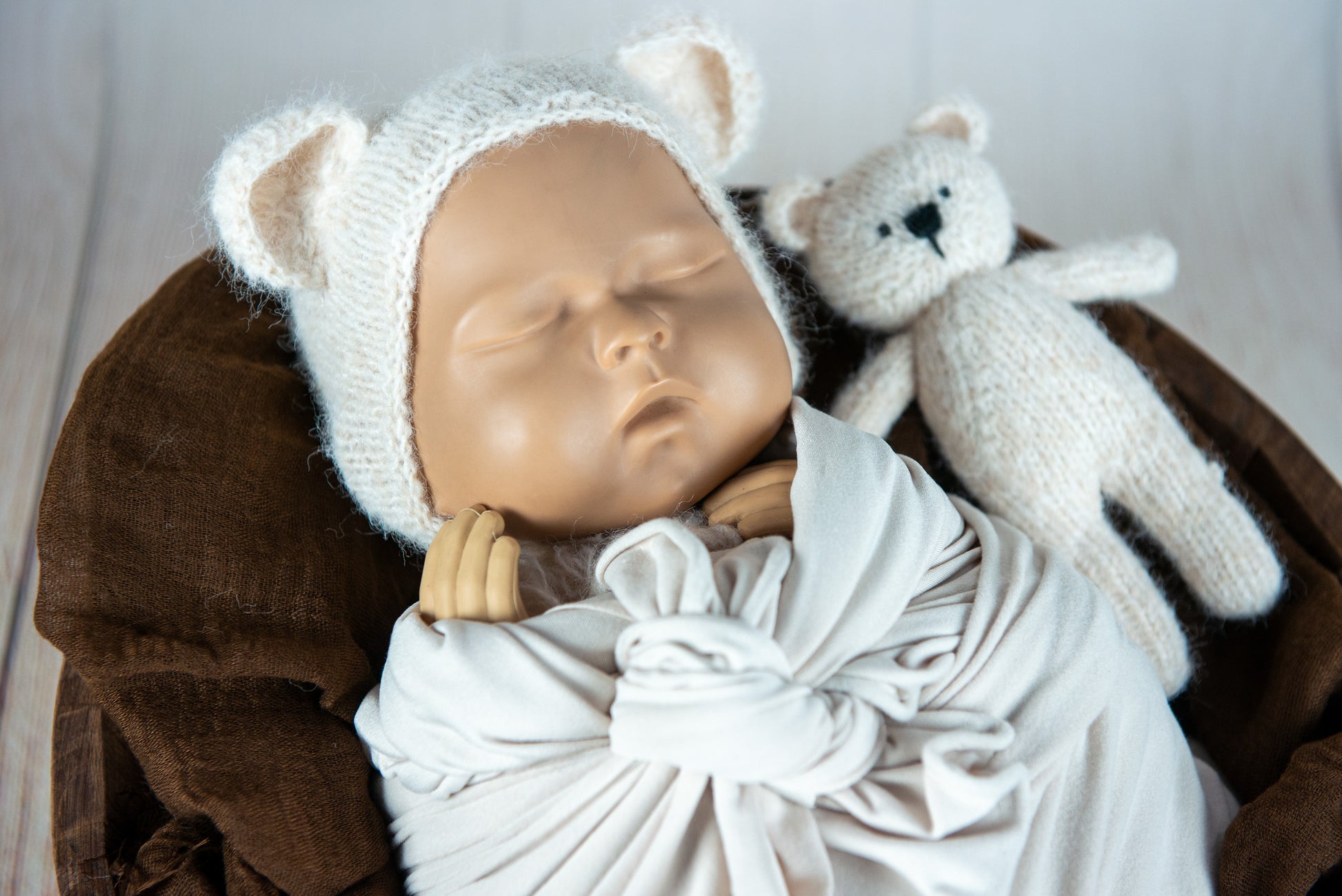 Knit teddy bear and matching hat beside cream swaddle; newborn photography prop.