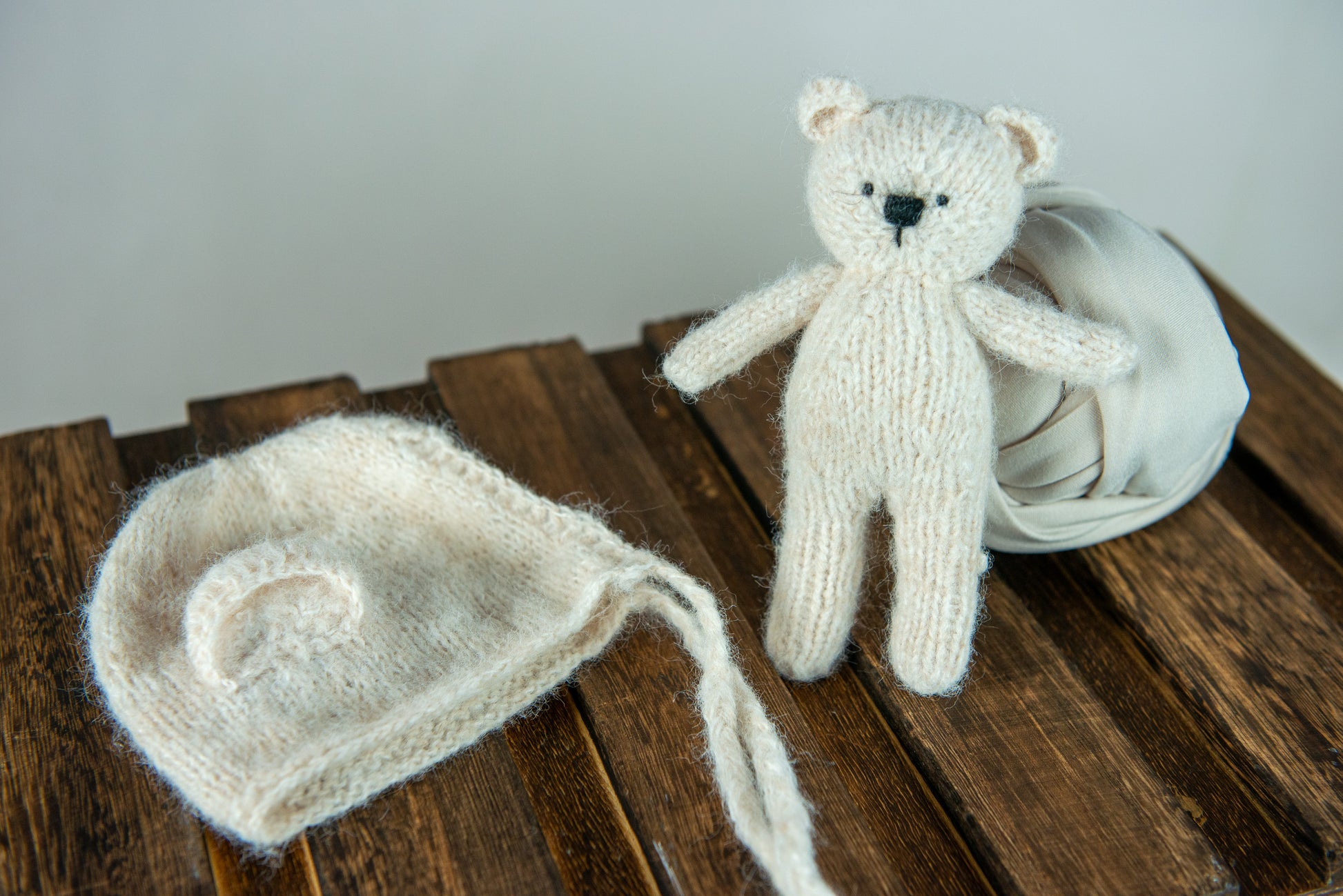 Knit teddy bear and matching hat beside cream swaddle; newborn photography prop.