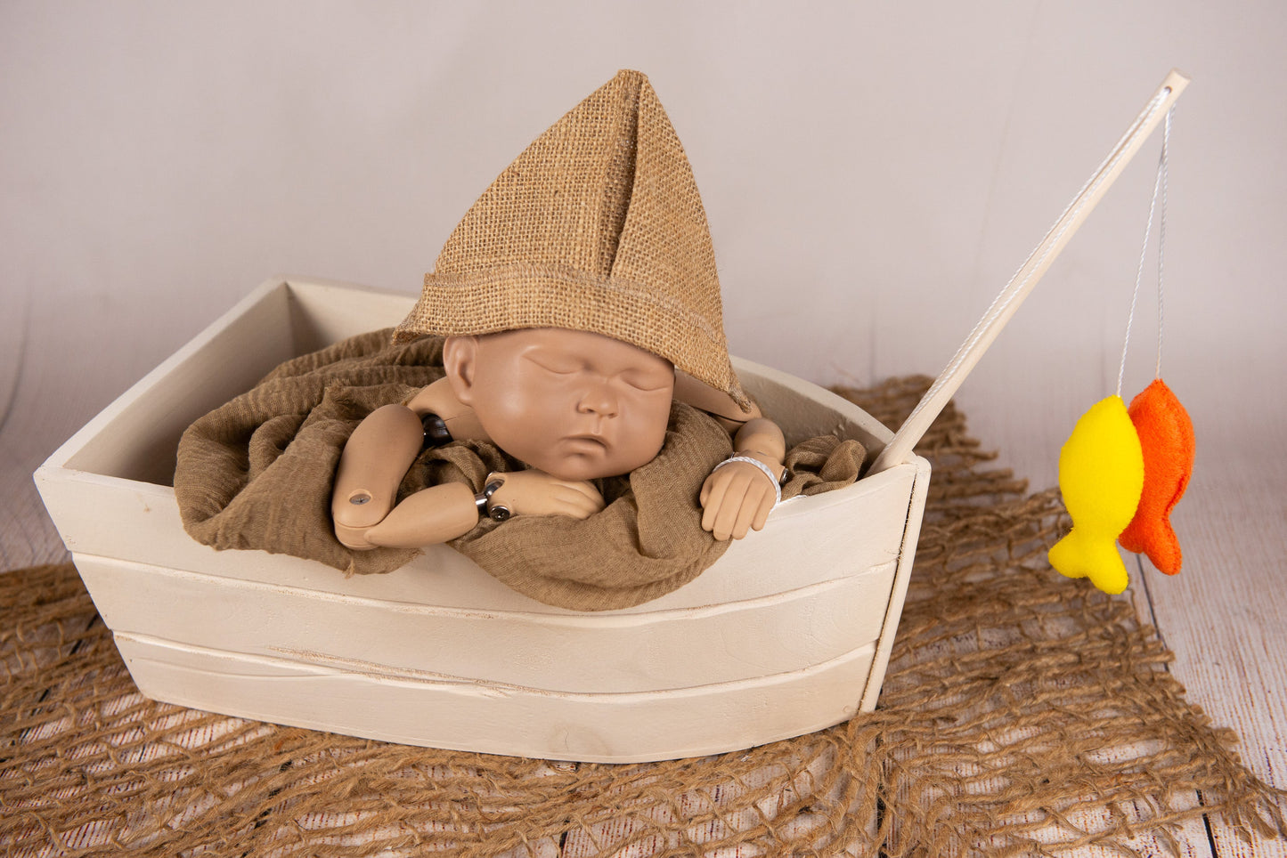 A faux fishing rod with orange and yellow felt fish on a rustic net, ideal for newborn photography prop setups.