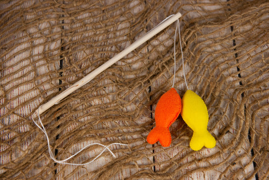 A faux fishing rod with orange and yellow felt fish on a rustic net, ideal for newborn photography prop setups.