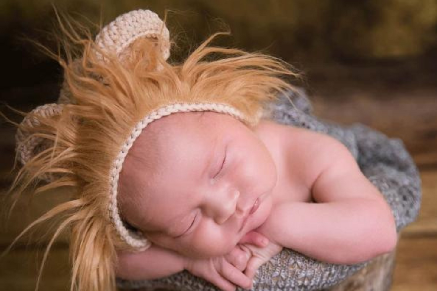 Newborn baby sleeping peacefully in a gray wrap, wearing the Lion Bonnet with Ears and Mane, a cozy newborn photography prop.