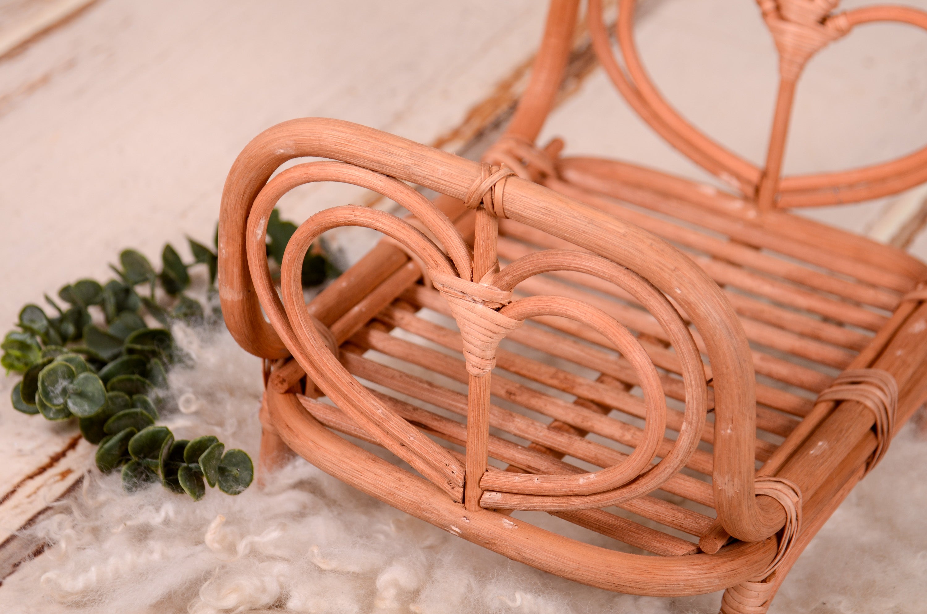 Rattan love nest newborn photography prop on a soft, fluffy rug.