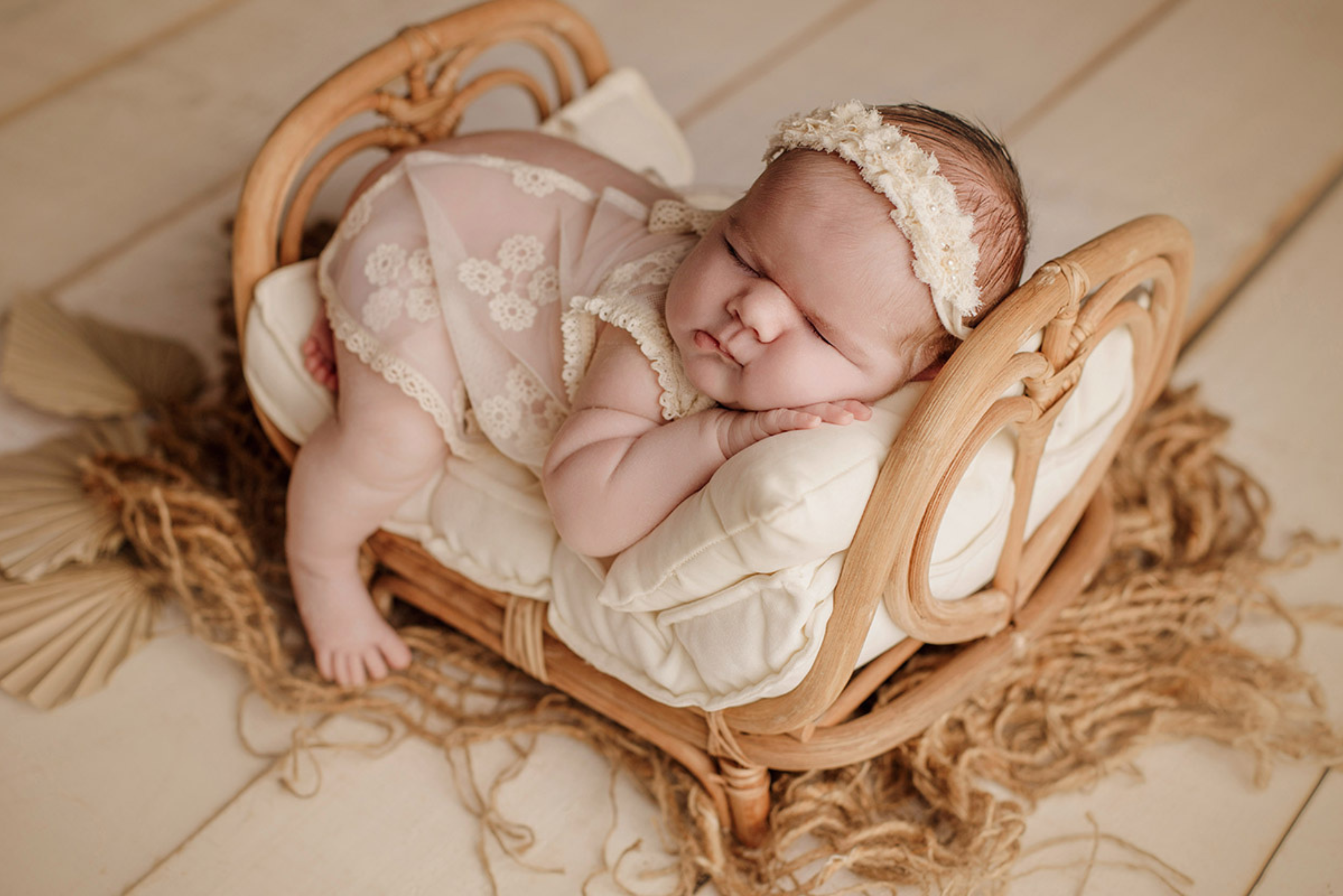 Newborn in a cozy rattan basket with fluffy white blanket, floral headband, and gentle backdrop.
