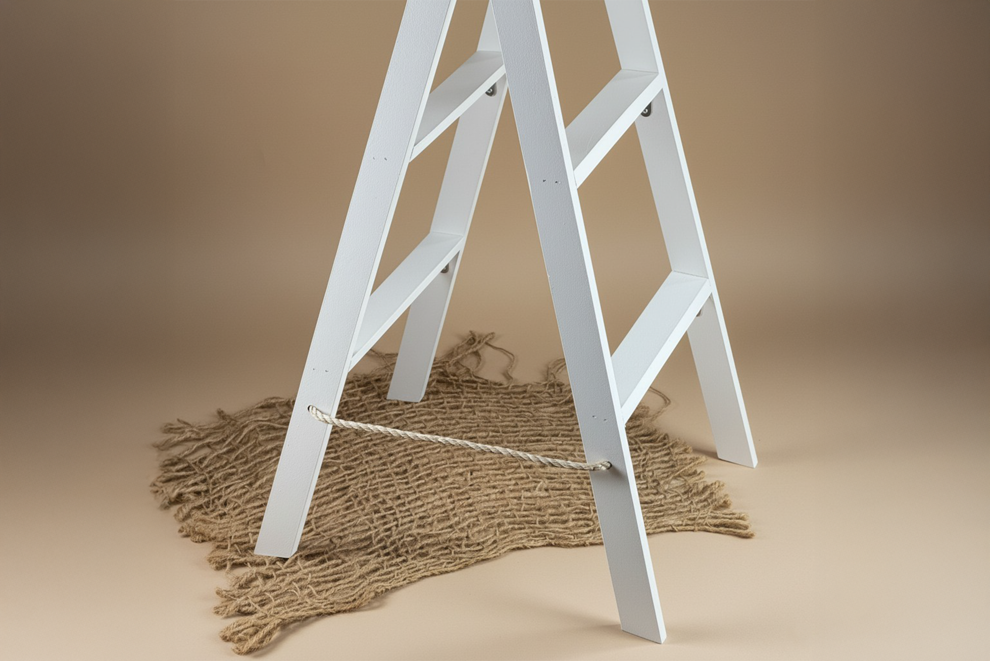 Close-up of white wooden ladder base on jute mat, a rustic newborn photography prop for cozy setups.