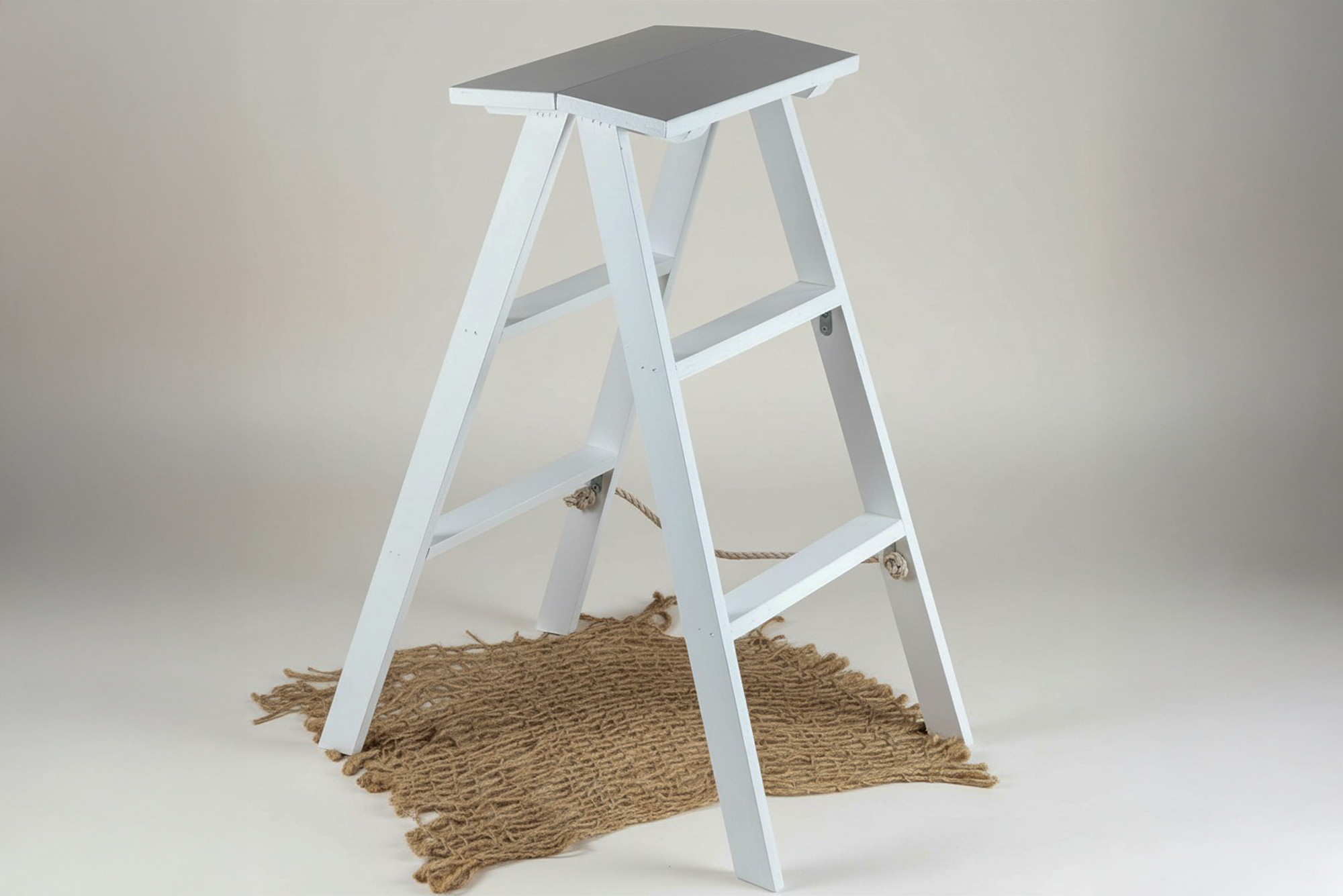 White wooden ladder styled on a textured jute mat, a versatile newborn photography prop for studio setups.