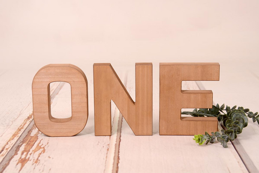 Brown wooden letters spelling out 'ONE' on a rustic wooden background, ideal for cake smashes or milestone photography.