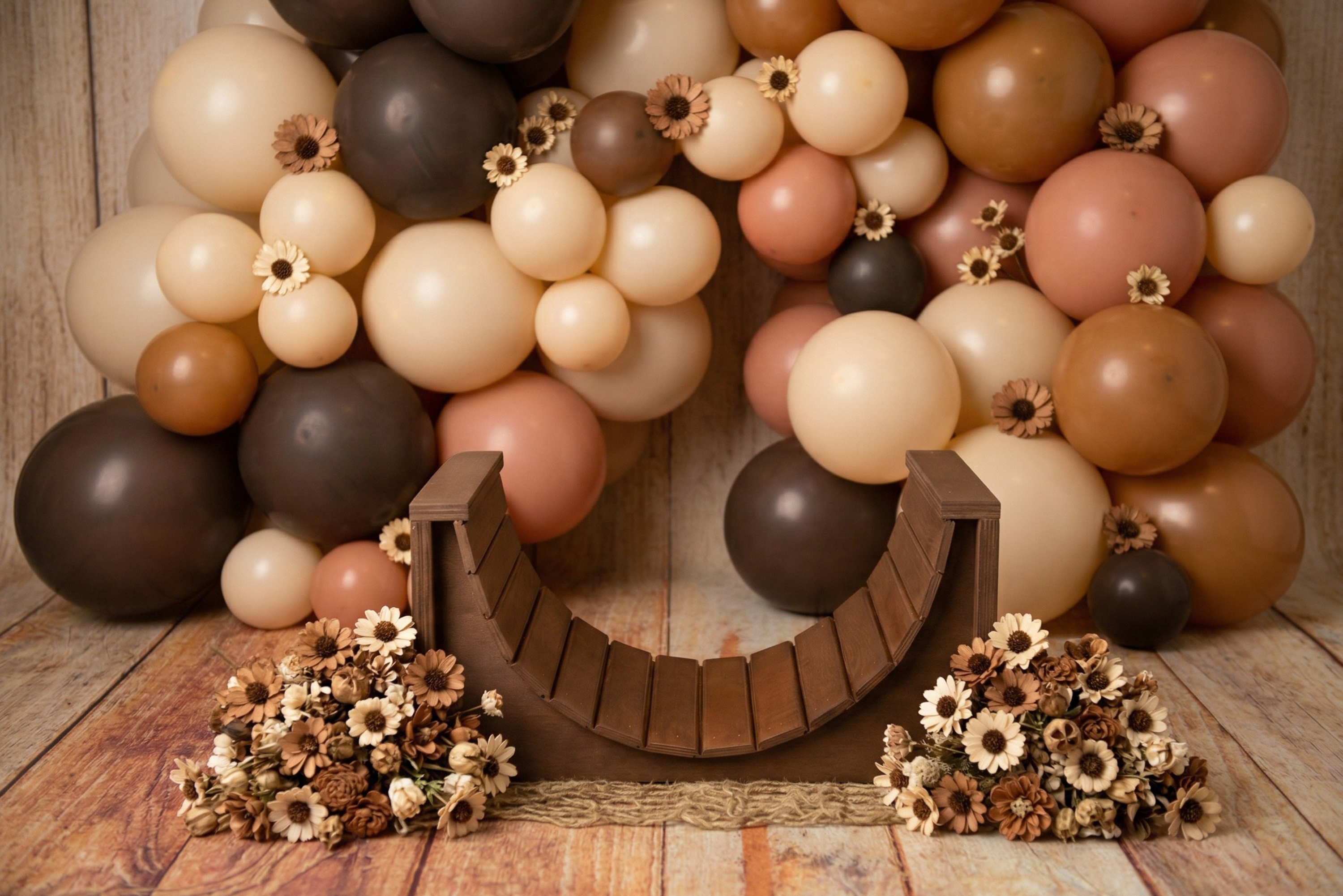 Balloon baby smash cake setup for photography. arch bench with brown, beige, and gold balloons on a wooden floor.