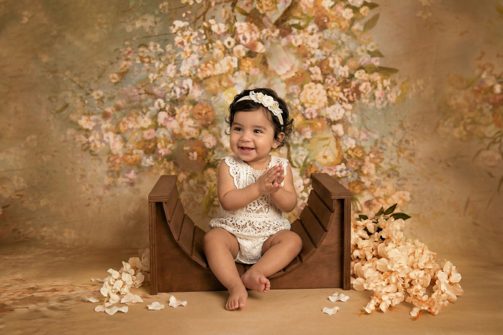 Baby sitting in a wooden crib arch lounger newborn prop with floral decorations and a brown background