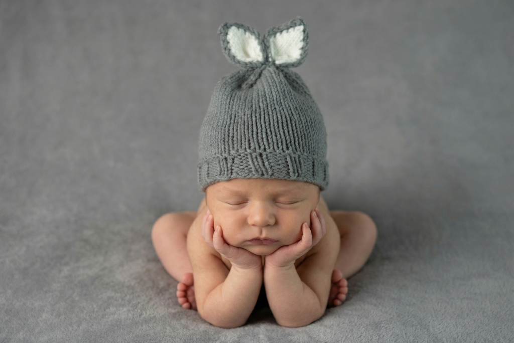 Newborn baby wearing a gray knit hat with bunny ears on a gray background