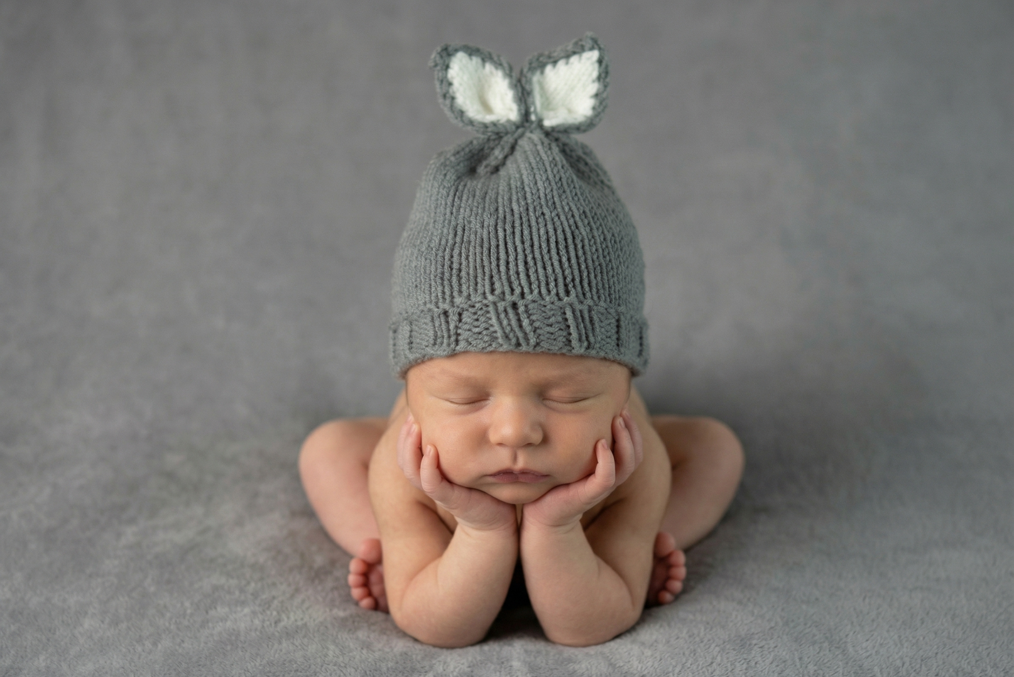 Newborn baby wearing a gray knit hat with bunny ears on a gray background