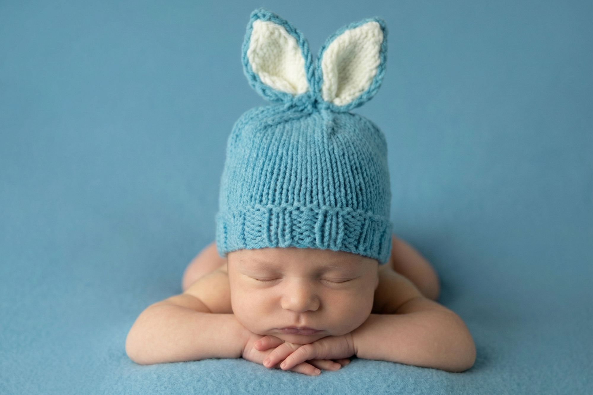 Newborn baby wearing a blue knitted hat with bunny ears on a blue background