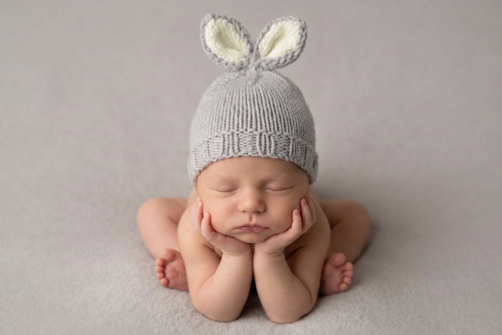 Newborn baby wearing a knitted gray hat with bunny ears on a plain background