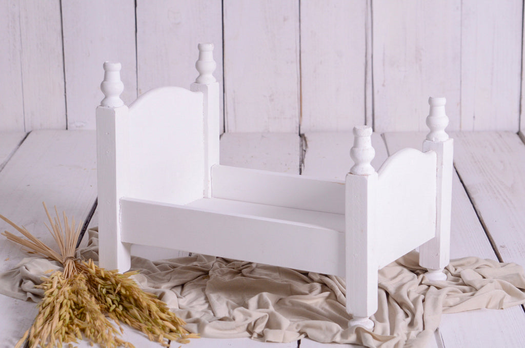 White vintage-style wooden bed on beige fabric with dried wheat, newborn photography prop.