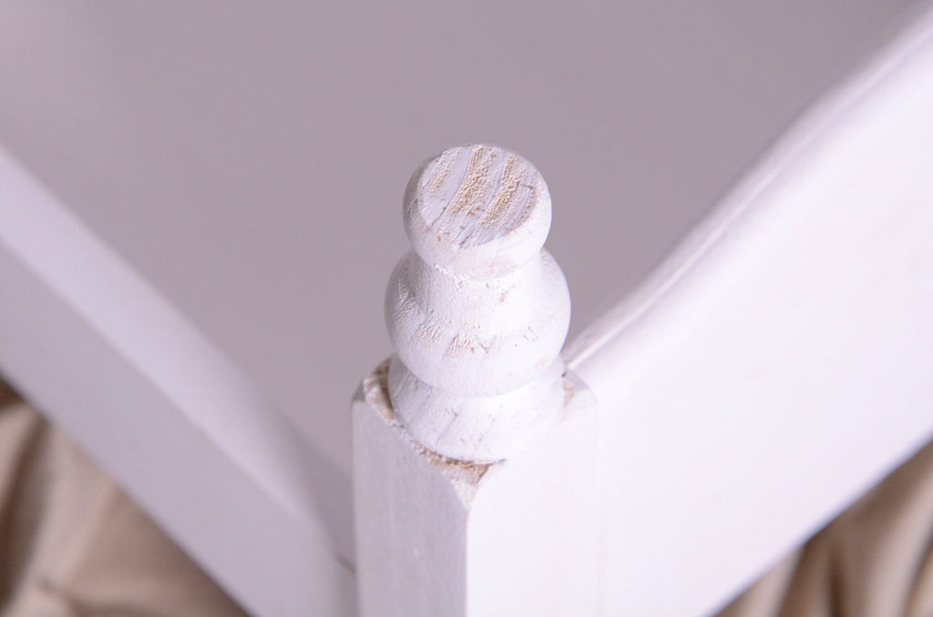Close-up of turned wood post on painted white mini bed, newborn photography prop detail.