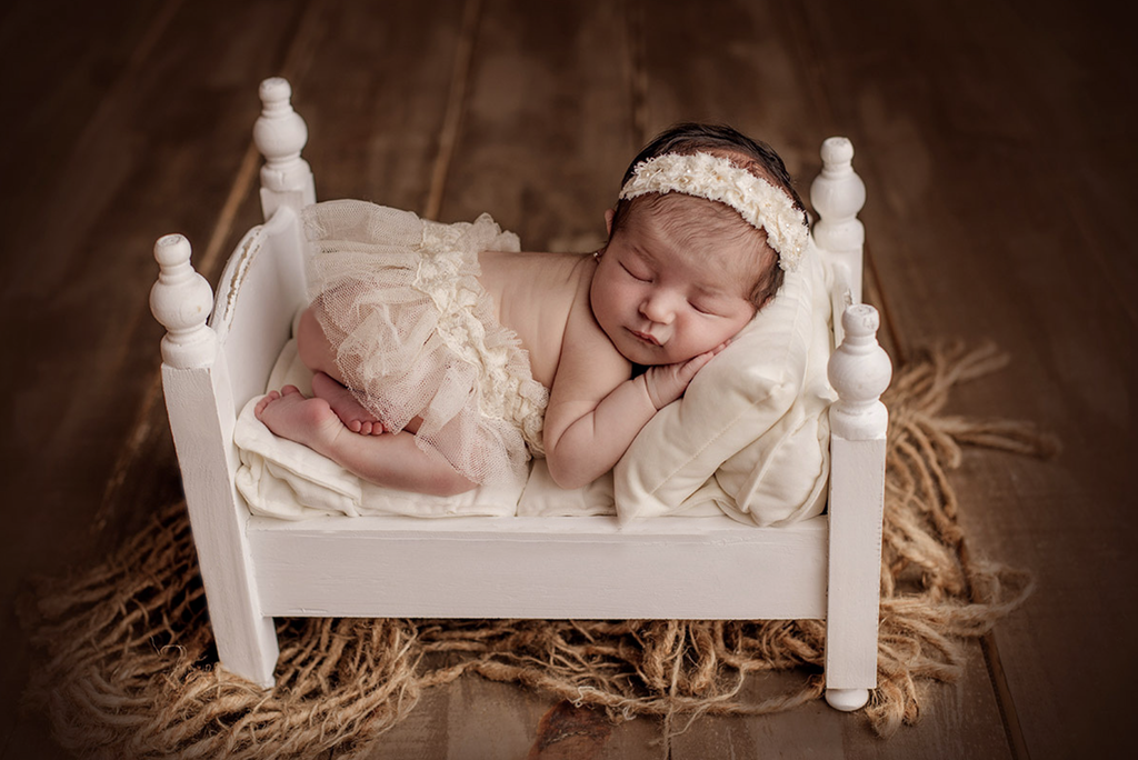 Sleeping newborn in white painted bed on rustic wood floor, vintage newborn photography prop.