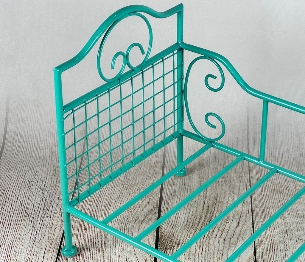 Charming green metallic wire bed for baby photography, complete with vintage-inspired patterns on a natural wood floor.