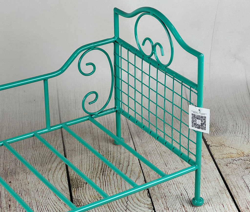 Intricately designed green vintage-style wire bed prop for photography, resting on a weathered wooden surface.