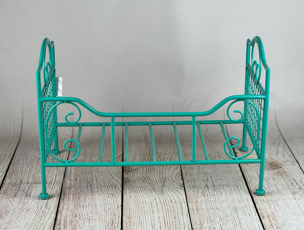 Newborn photography prop featuring a green metal bed with swirled details, set against a rustic wooden background.