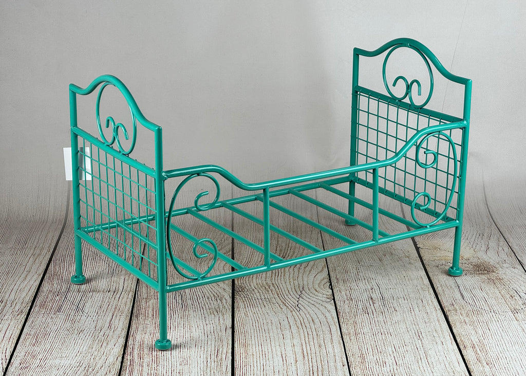Ornate green wire frame bed, designed for newborn photography sessions, displayed on a wooden plank floor.