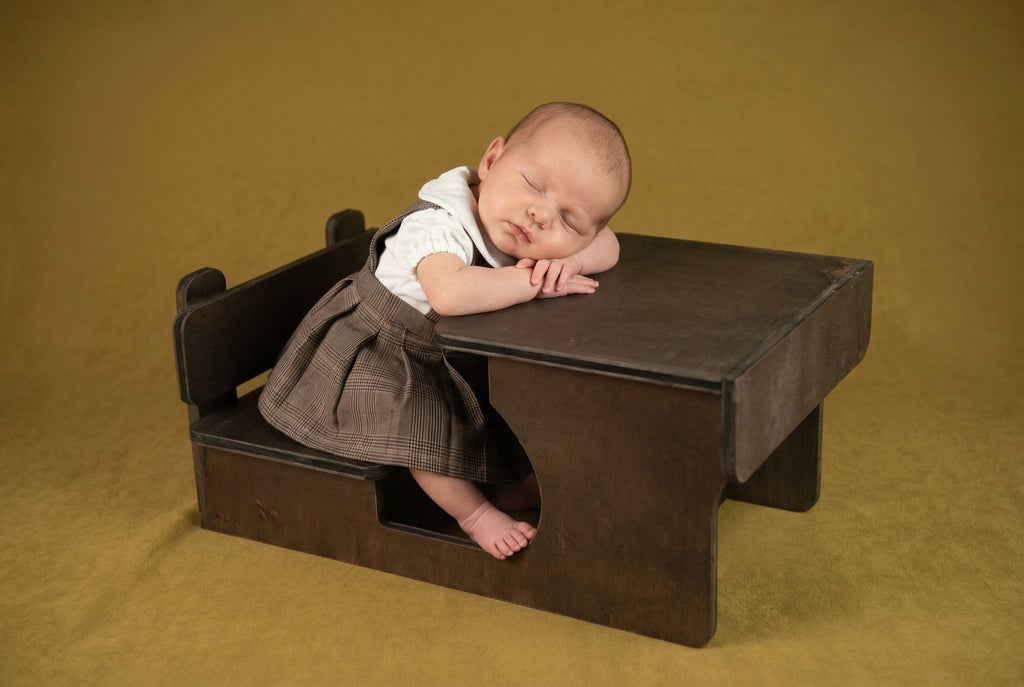Newborn baby sleeping on a small brown school desk prop against a beige background