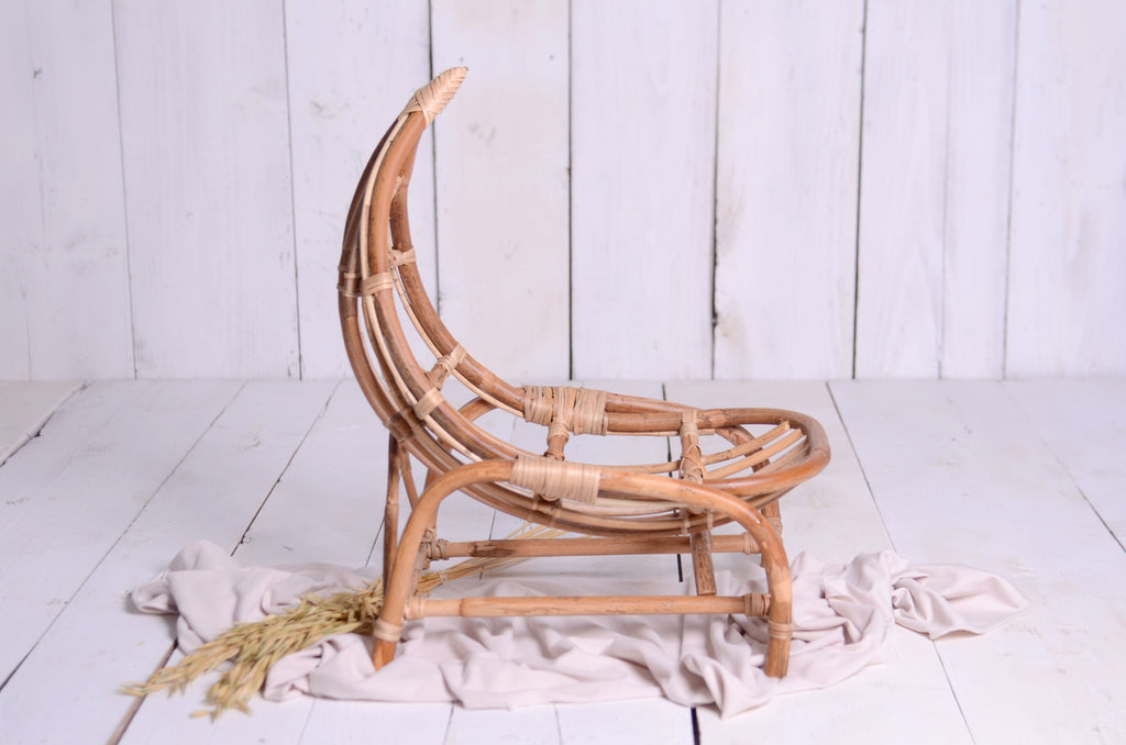 Rustic rattan crescent moon newborn photography prop on a white wooden backdrop, styled with a soft beige fabric and dried wheat for a dreamy, natural setup.