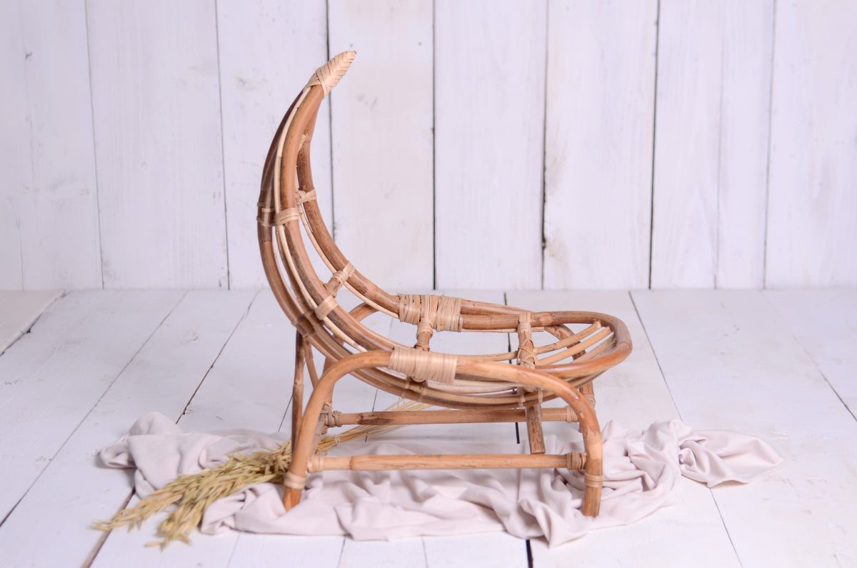 Rustic rattan crescent moon newborn photography prop on a white wooden backdrop, styled with a soft beige fabric and dried wheat for a dreamy, natural setup.