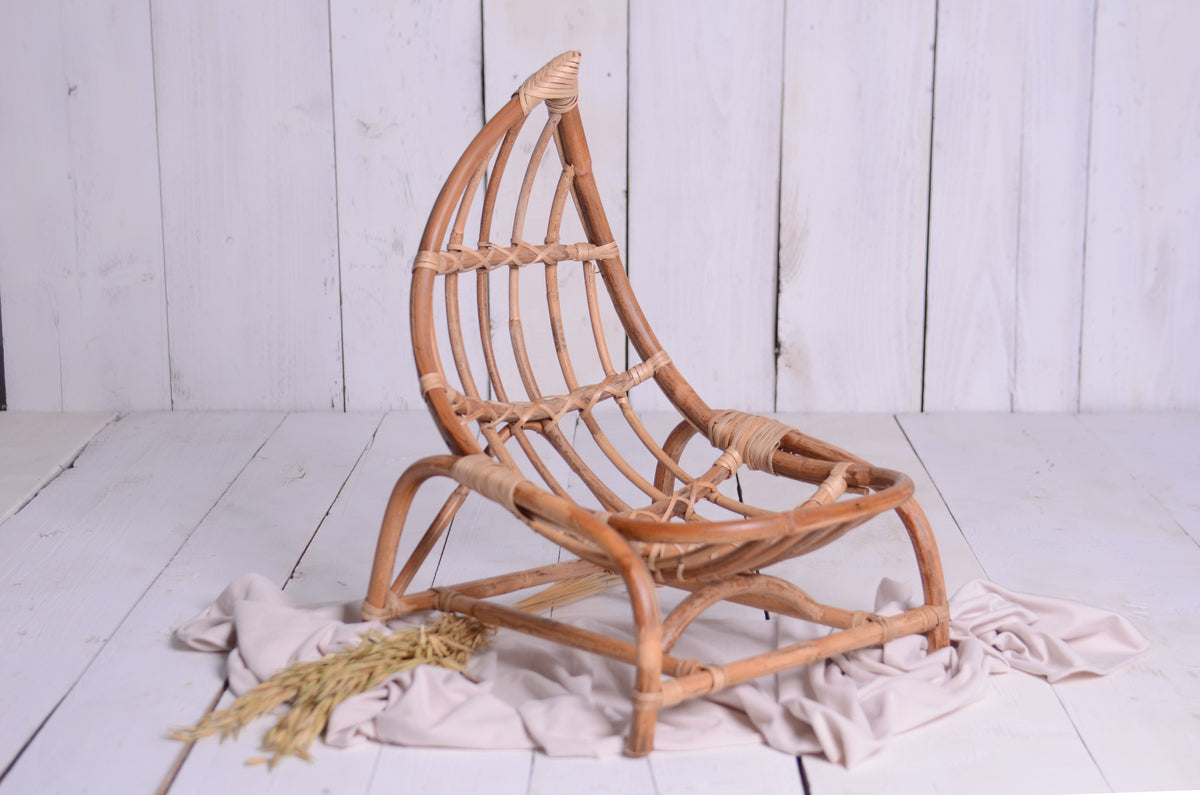 Boho-style crescent moon newborn photography prop made of natural rattan, set against a white wooden backdrop with delicate fabric draping and wheat stalks for a warm, organic feel.