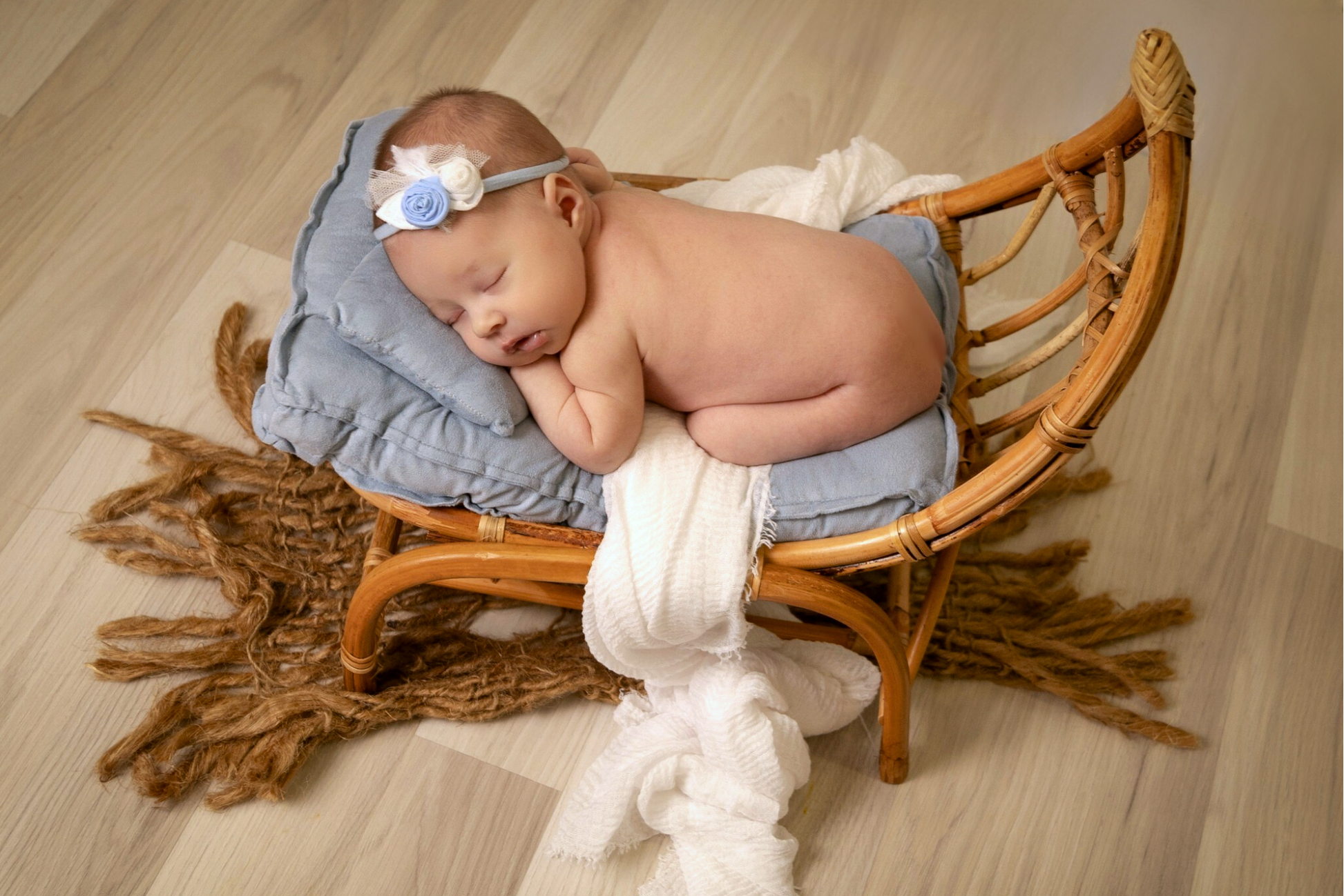 Newborn photography prop: A half-moon rattan hammock chair with soft blue cushions, cradling a sleeping baby.