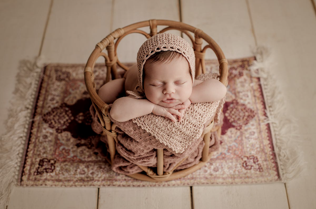 A sweet baby poses in a LovePod rattan basket, styled with earthy tones and carpet—a must-have newborn photography prop.
