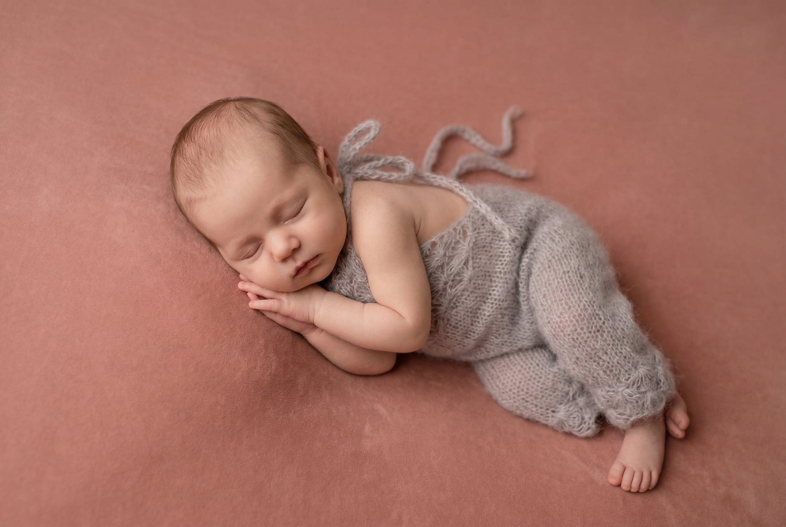 Newborn baby in a gray knitted outfit lying on a pink blanket