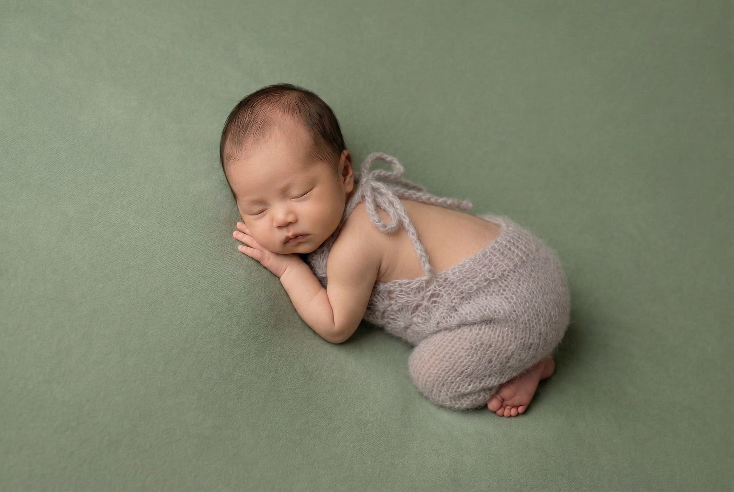Newborn baby in a gray outfit sleeping on a green background