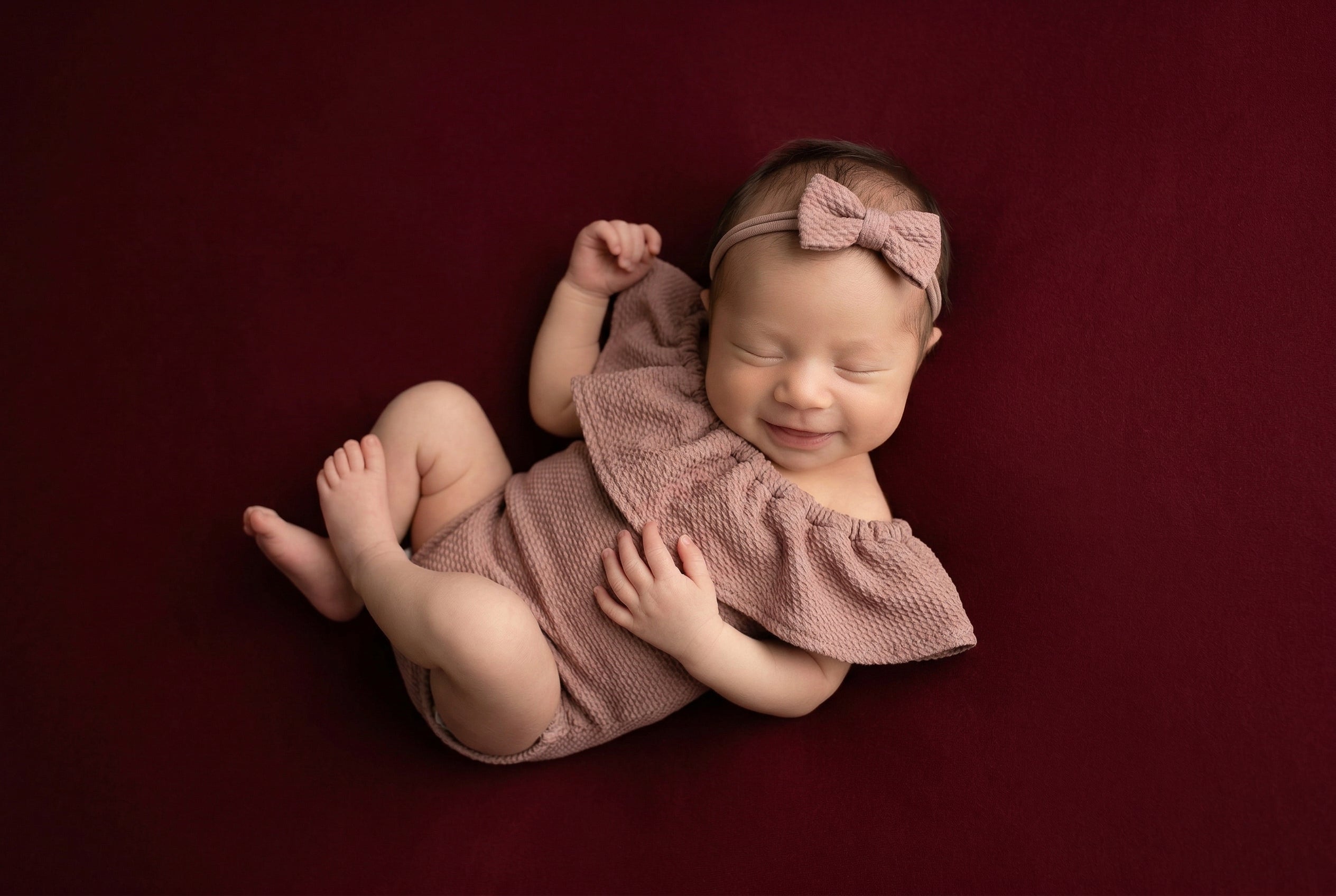 Newborn baby in a pink outfit and headband on a red background