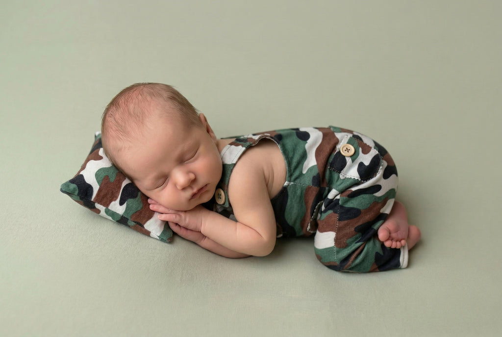 Newborn baby in a camouflage outfit lying on a light green background