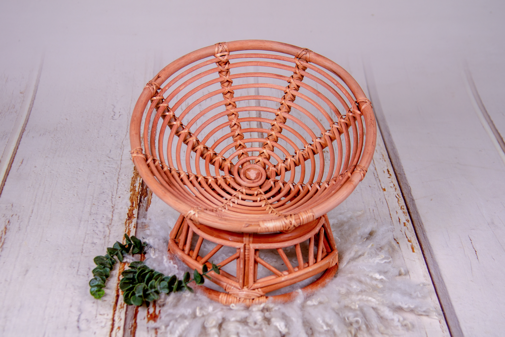 Top-down view of papasan rattan bed newborn photography prop with textured wool layer and eucalyptus sprig.