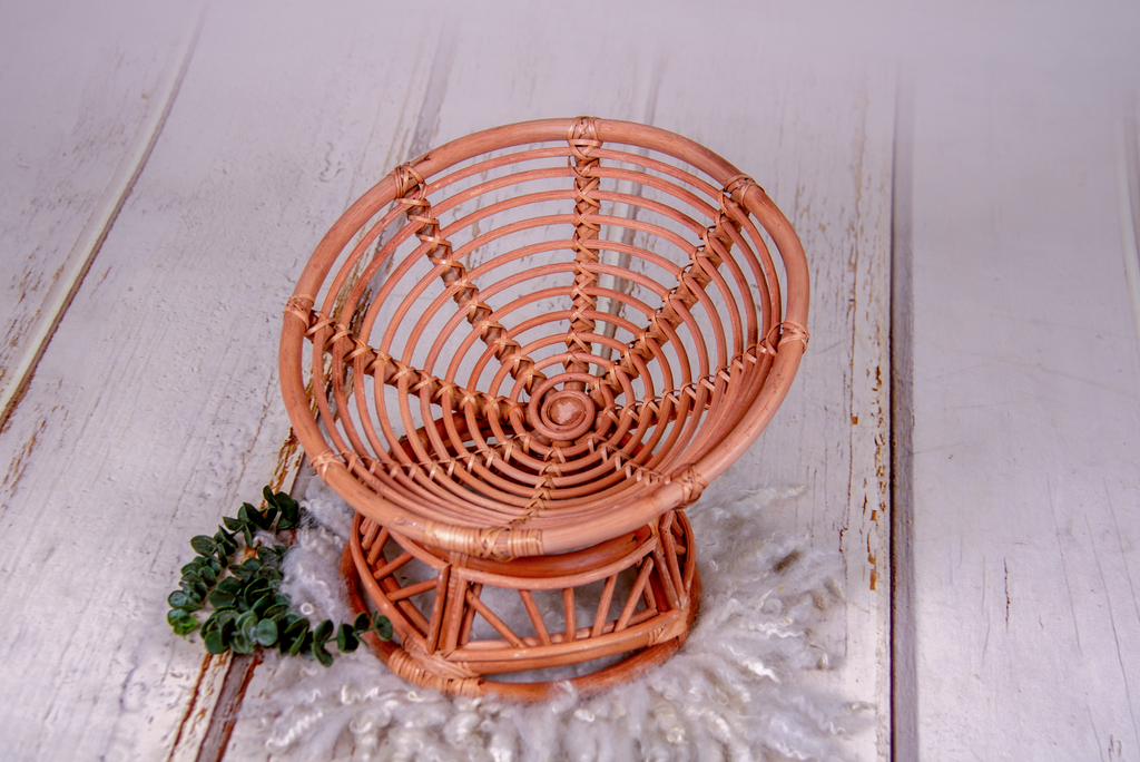 Fully assembled rattan bowl papasan chair newborn photography prop set on white wood floor with wool and greenery.