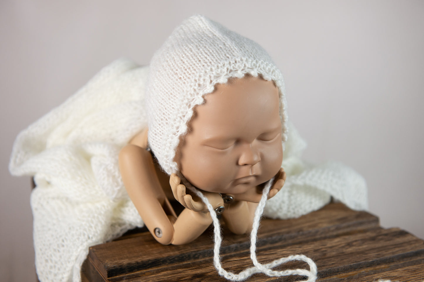 Sleeping doll in gray knit bonnet with matching wrap as cozy newborn photography prop.