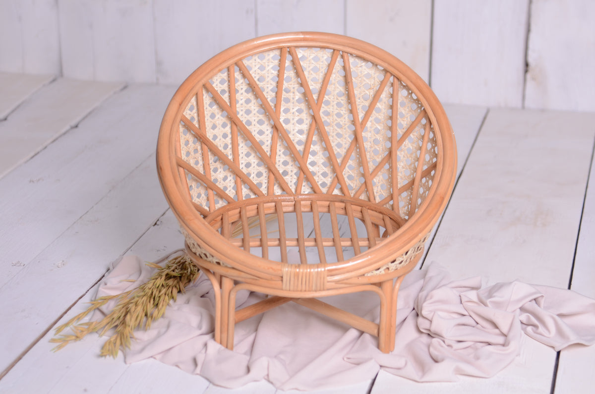 Front-facing view of a rattan nest cocoon newborn photography prop, featuring a round woven backrest and natural cane detailing, styled with neutral fabric and wheat accents.