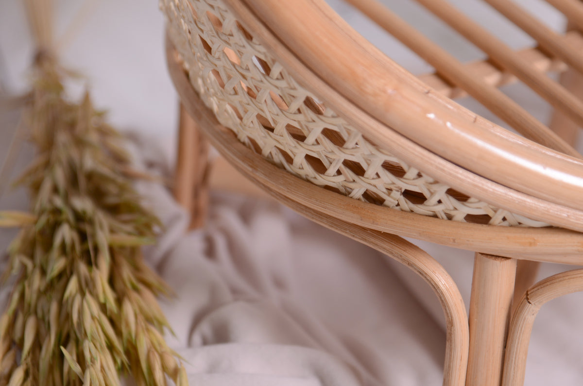 Detailed shot of the lower frame of the rattan nest cocoon newborn photography prop, highlighting the curved rattan legs and woven cane trim against a soft fabric backdrop.