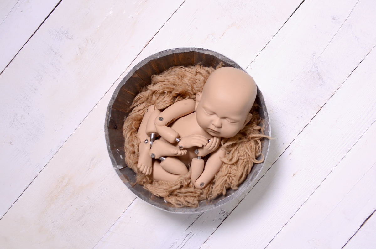 Newborn baby posed in a wool-lined bowl, highlighting a white wooden floor as a newborn photography prop.