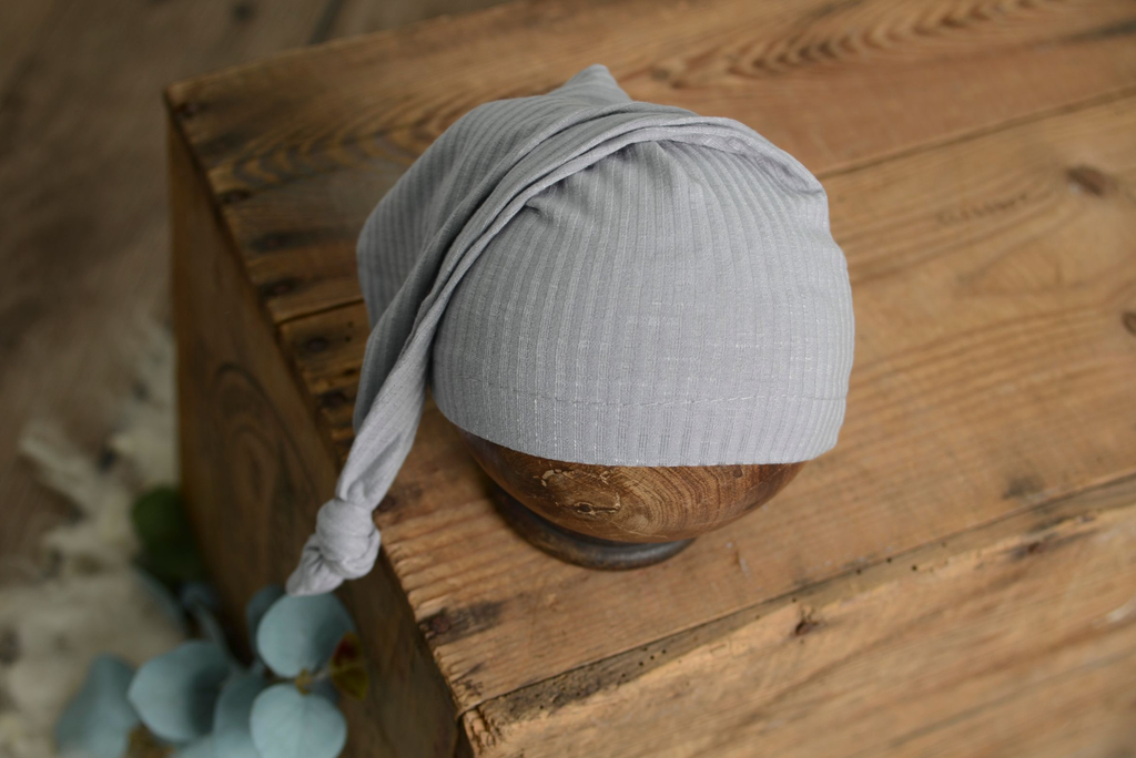 Light gray ribbed knot sleepy cap newborn photography prop styled on wooden bowl with rustic detail.