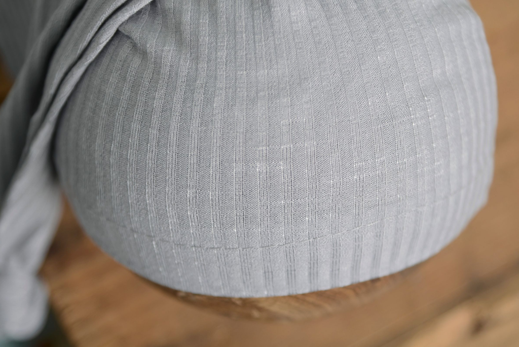Light gray ribbed knot sleepy cap newborn photography prop close-up on rustic wooden bowl.