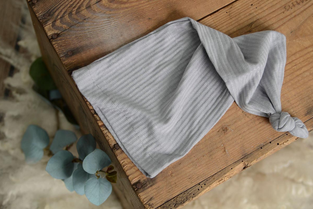 Light gray ribbed knot sleepy cap newborn photography prop displayed flat on rustic wood.