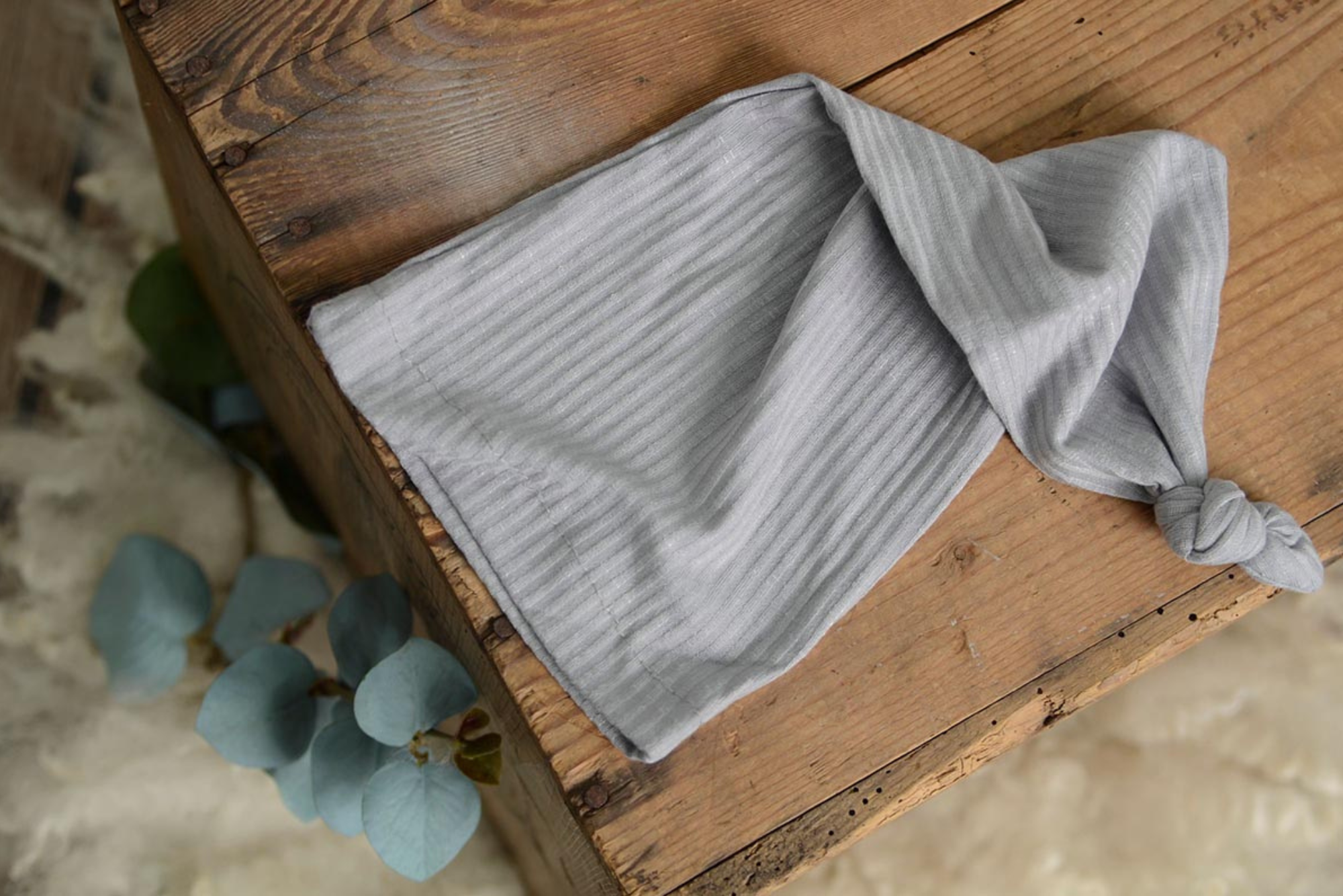 Light gray ribbed knot sleepy cap newborn photography prop displayed flat on rustic wood.