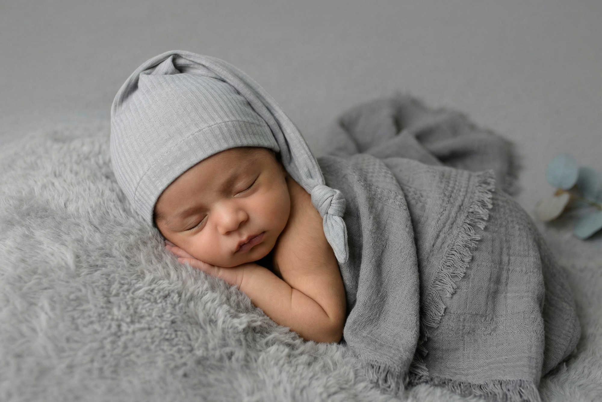 Sleeping newborn in gray wrap with ribbed knot sleepy cap newborn photography prop on soft blanket.