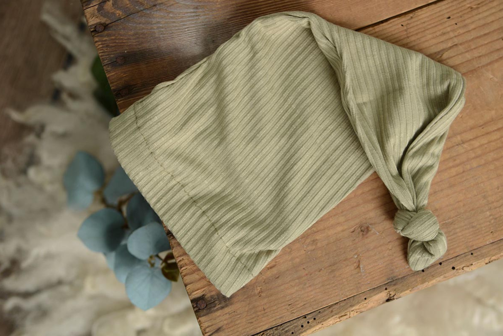 Sage green ribbed knot sleepy cap newborn photography prop displayed flat on rustic wood.