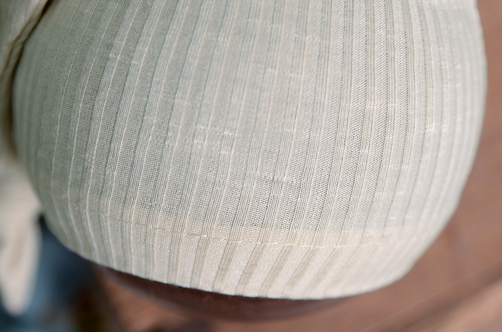 Close-up of cream newborn photography prop sleepy hat showing soft ribbed texture and stretch fabric.