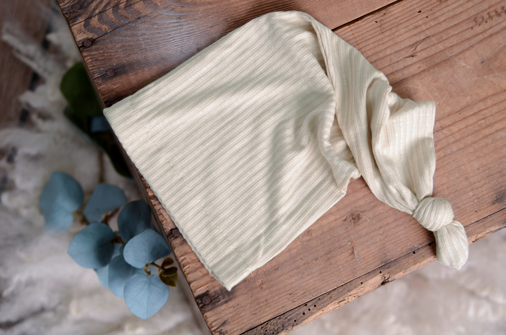 Cream ribbed newborn photography prop sleepy hat laid flat on rustic wood with soft blue florals.