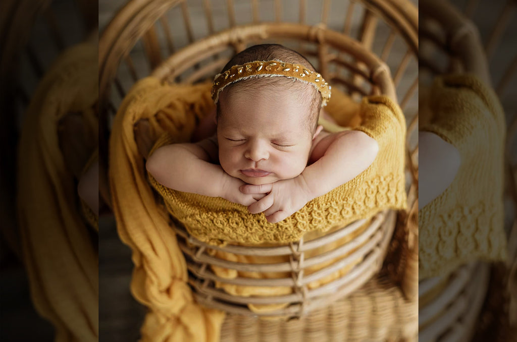 Nestled inside a rustic rattan bowl, this sweet newborn sleeps soundly, enveloped in a cozy mustard wrap. The natural textures of the woven basket and warm wooden floor create a charming, organic setting, making this the perfect prop for capturing precious first moments.