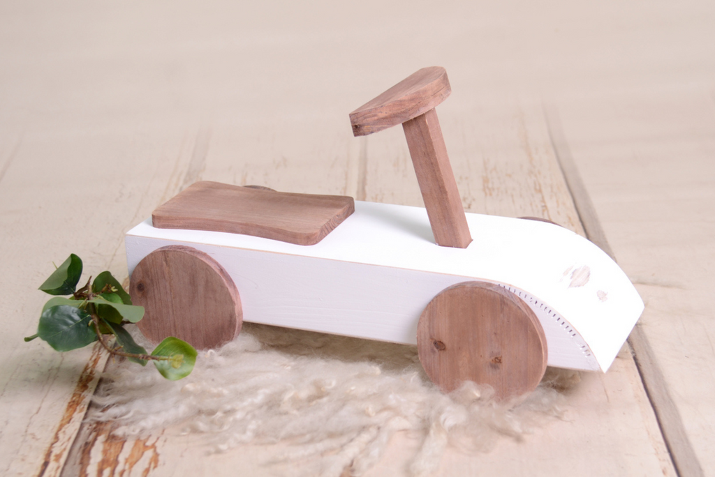 Close-up of the Rustic Ride-On - White, styled with a small wooden "1" and greenery, set on a neutral backdrop for a timeless newborn photography prop setup.