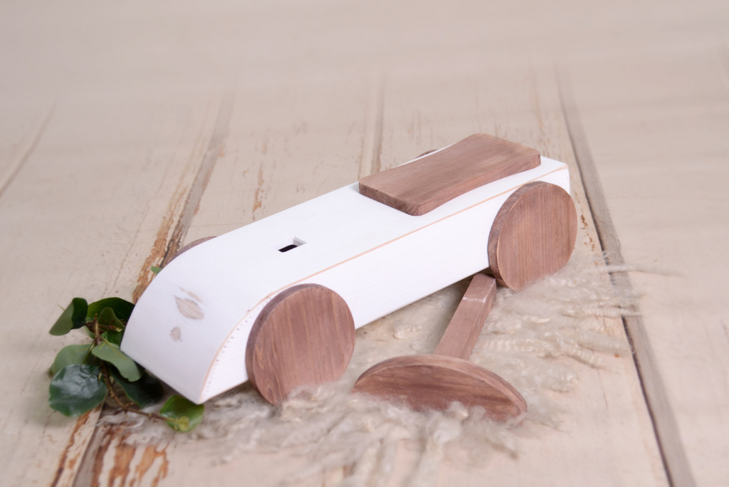 Side angle of the Rustic Ride-On - White, showcasing its wooden wheels and distressed white finish, a charming newborn photography prop.